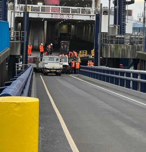 Dock workers looking at a truck on a loading ramp on a boat 