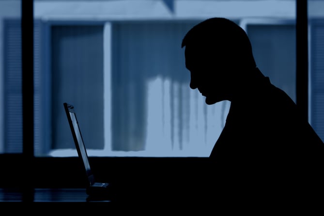 Generic image of a man silhouetted and hunched over a computer