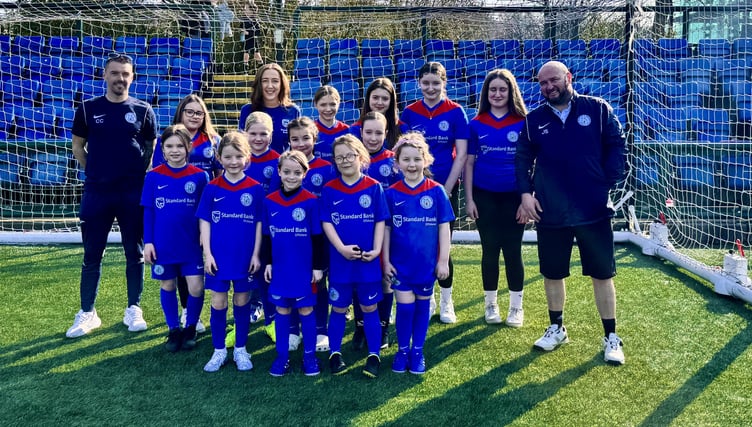 Douglas and District FC's girls’ team with coaches Chris Coxon (left) and Micky Corlett (right) alongside Catherine Harrop from Standard Bank Offshore