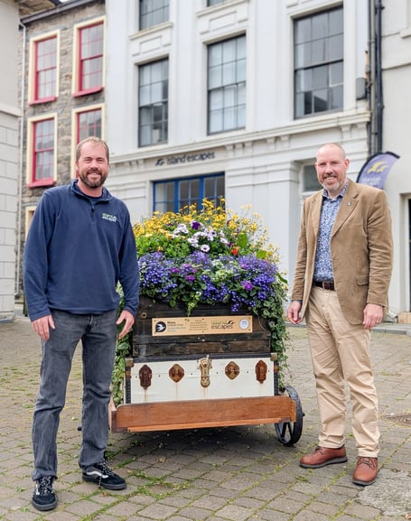 John Keggin, managing director of Island Escapes, and Graham Makepeace-Warne, chief executive of Manx Wildlife Trust, with the flower-adorned luggage cart outside Island Escapes’ Castletown office