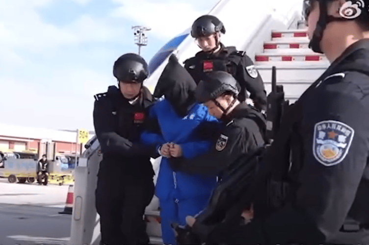 A hooded and handcuffed Chen Zhi is led down the steps of the aircraft at Beijing