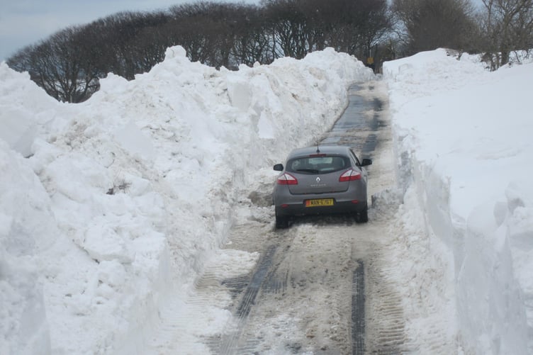 A car drives up a road enclosed by banks of snow in 2013