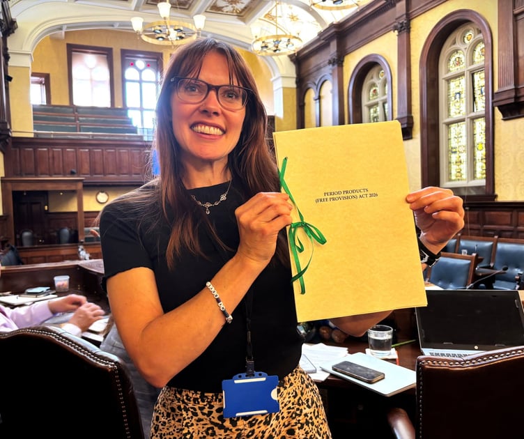 Joney Faragher holding the Period Products (Free Provision) Act 2026 in the House of Keys